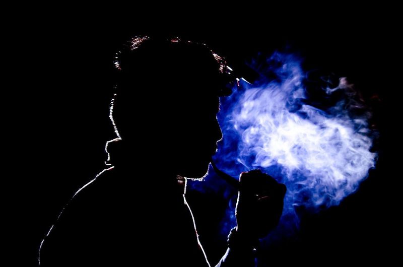 Full length portrait of silhouette man smoking against black background