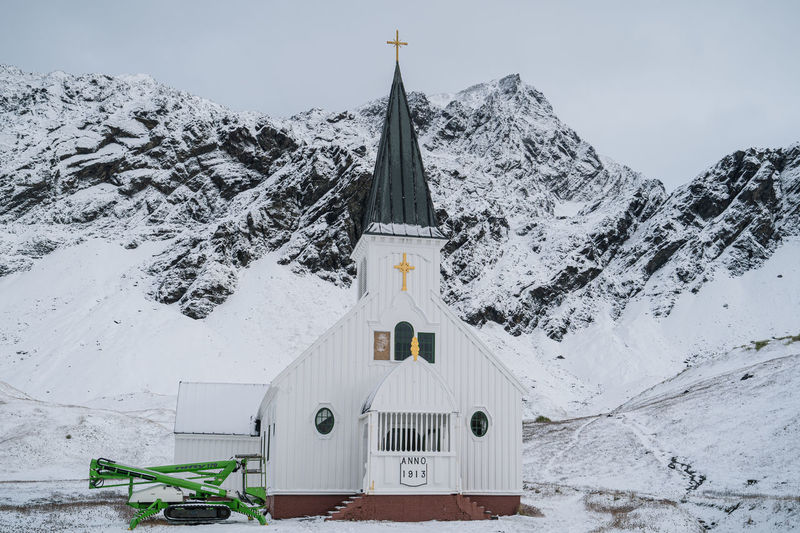Snow covered church and mountains against sky