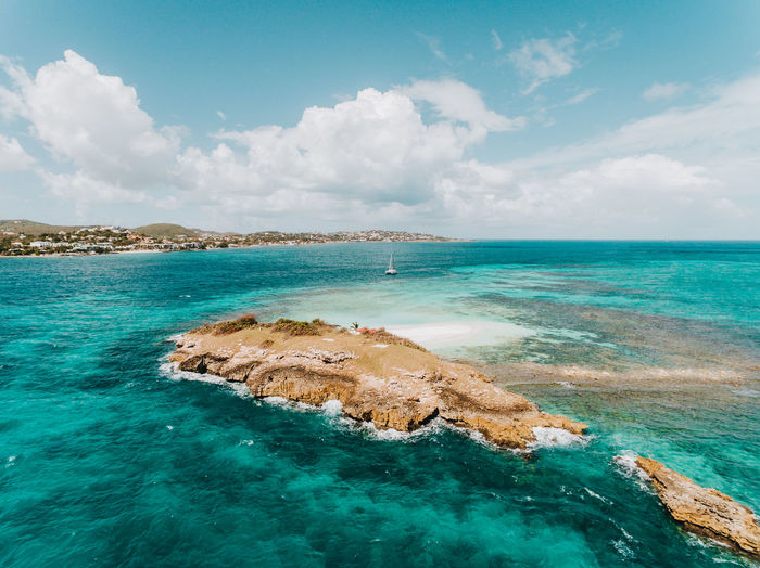 Prickly pear island in antigua with a sailing yacht in the distance and mainland antigua. 