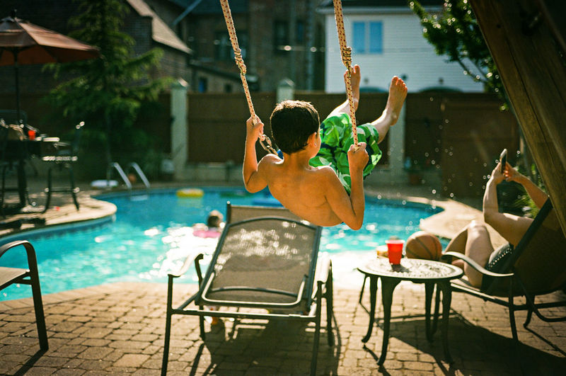 Rear view of boy playing on swing at poolside