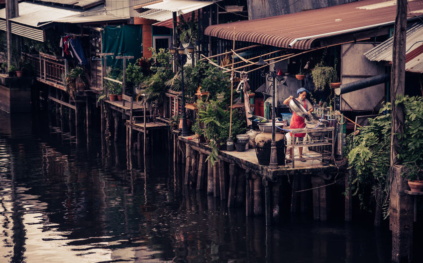 A woman washing dishes behind a shop next to a canal.