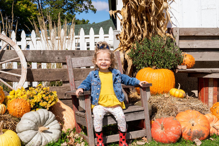 Portrait of smiling girl sitting on chair by pumpkins