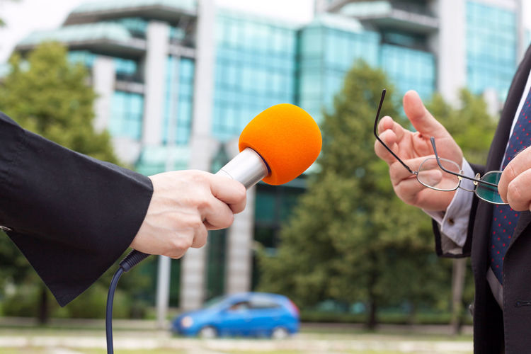 Cropped hand of journalist interviewing businessman in city