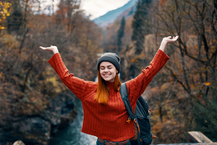 Smiling young woman with arms raised standing in autumn leaves