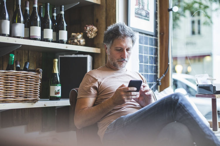 Mature owner using smart phone while sitting on chair in deli
