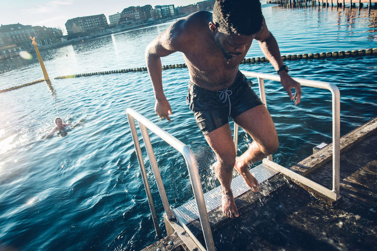 Young multiracial man coming out of cold water after swim in denmark