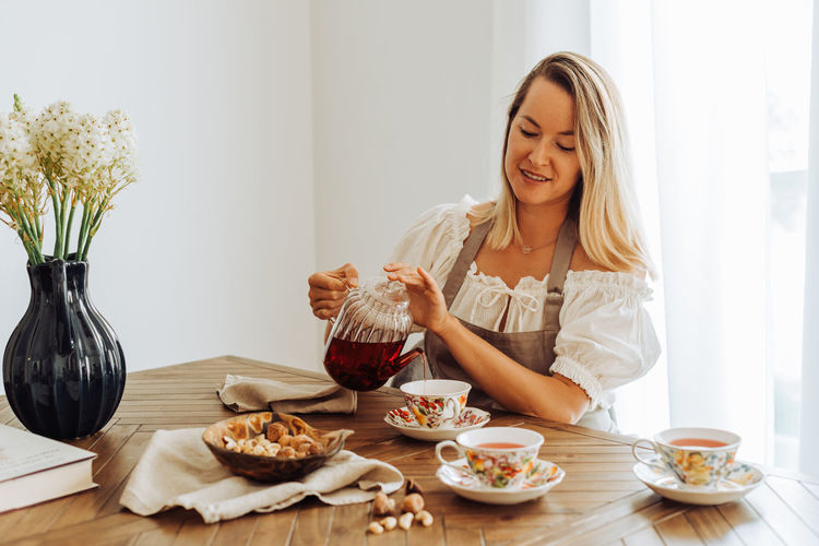 Blond woman pouring hibiscus tea in cups while sitting at table