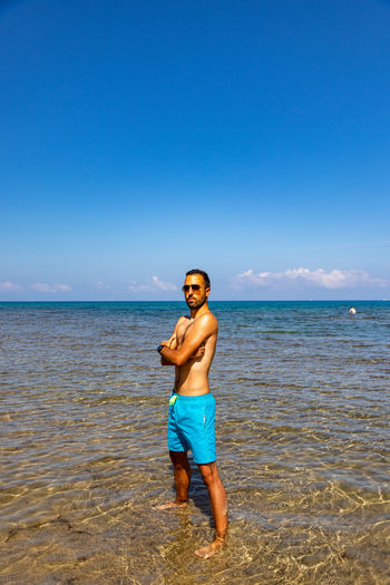 Full length of shirtless man standing on beach in castelsardo
