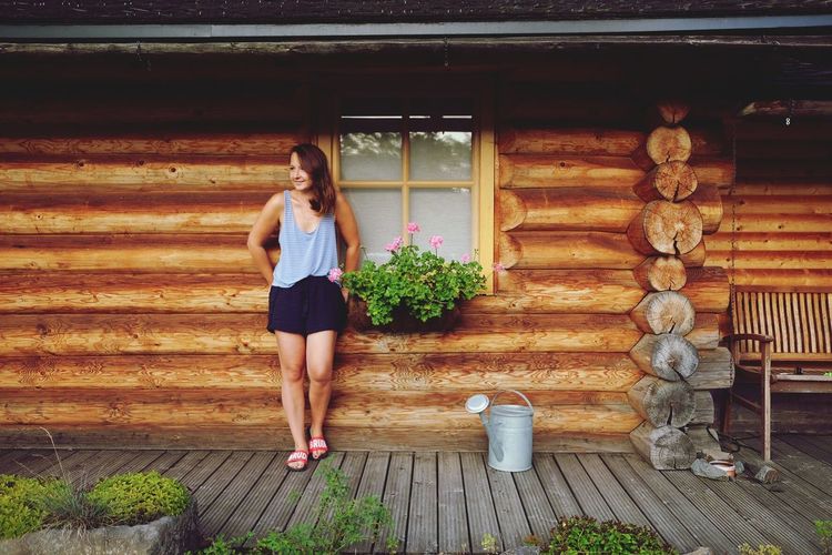 Full length of woman standing against log cabin