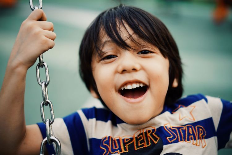 Close-up portrait of smiling boy swinging in playground