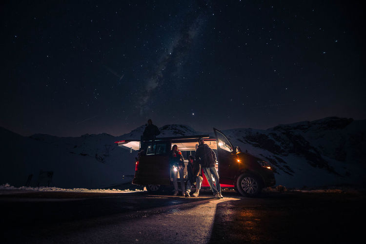 People with illuminated van against sky at night