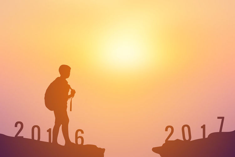 Silhouette boy with backpack standing on rock with numbers against sky during sunset
