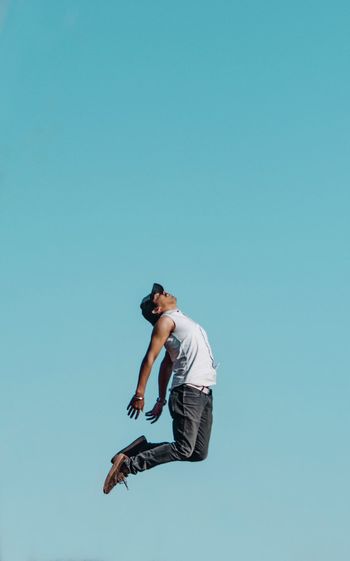 Low angle view of man jumping against clear blue sky