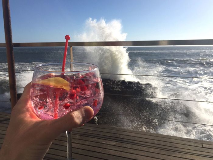 Close-up of hand holding wine glass against sea