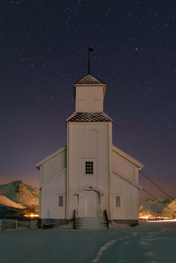 Church on snow covered land against sky at night