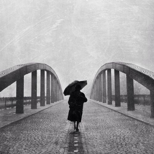 Person with umbrella walking on bridge against clear sky