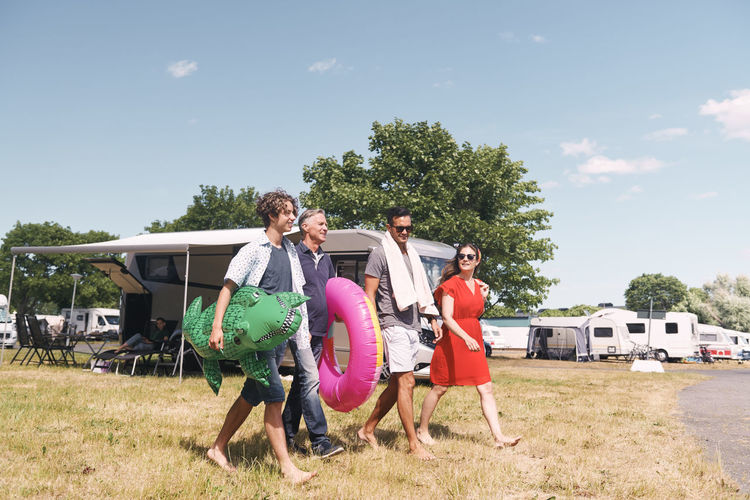 Full length of family with inflatable rings walking on grassy field against sky