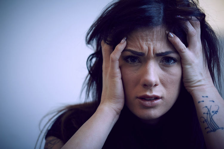 Portrait of depressed woman with hands in hair against wall