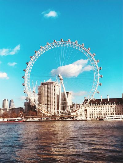 Millennium wheel by river in city against blue sky