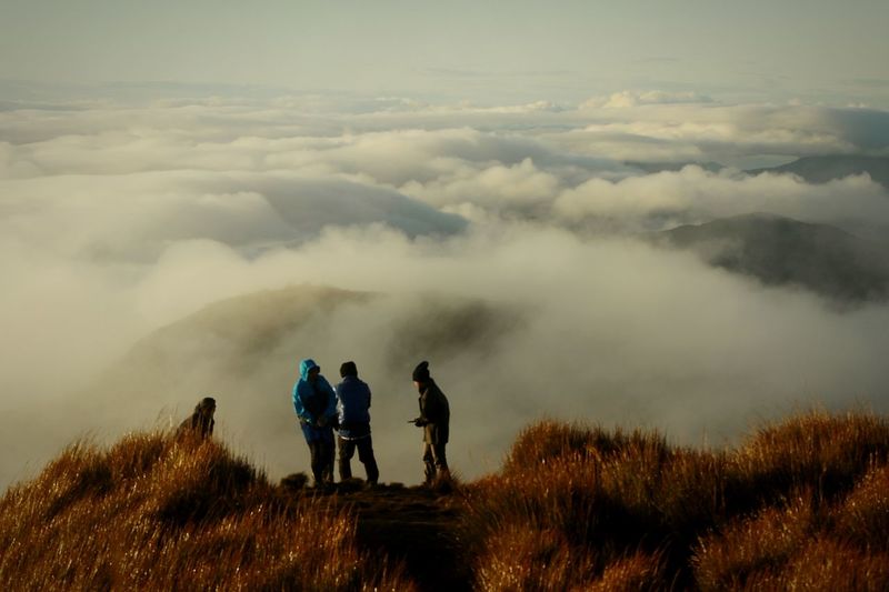 Hikers standing on mountain by cloudscape against sky