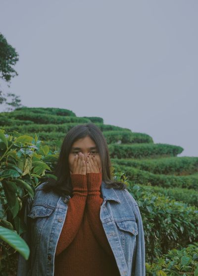 Woman covering mouth while standing against plants and sky