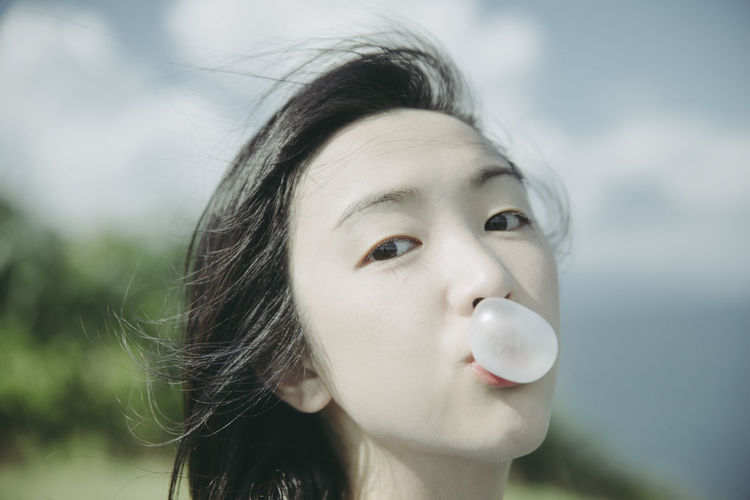 Close-up portrait of young woman blowing bubble gum