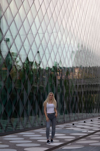 Full length portrait of woman standing on footpath against building