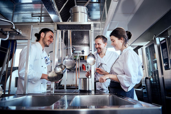 Smiling male and female chefs cooking food in commercial kitchen