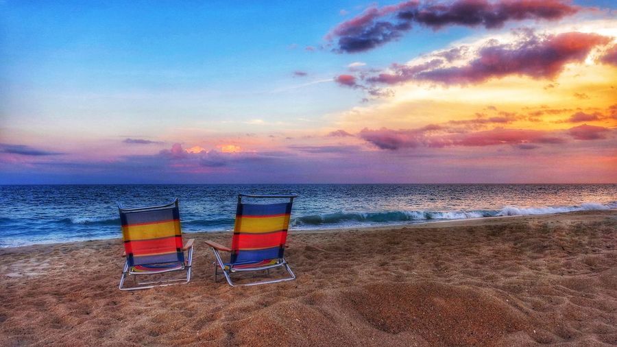 Deck chairs on beach against sky during sunset