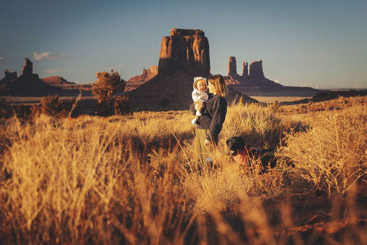A woman with a baby and a dog is standing in monument valley, arizona