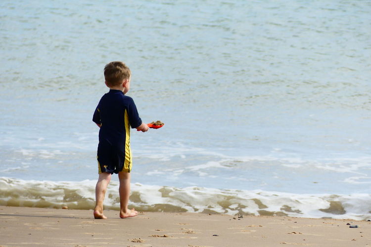 Rear view of boy playing on shore at beach