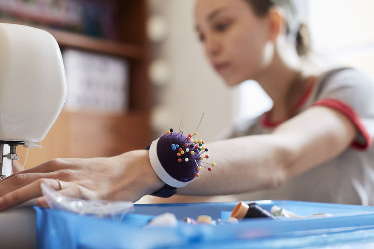 Close up of female tailor wearing pin cushion on wrist while using sewing machine at table
