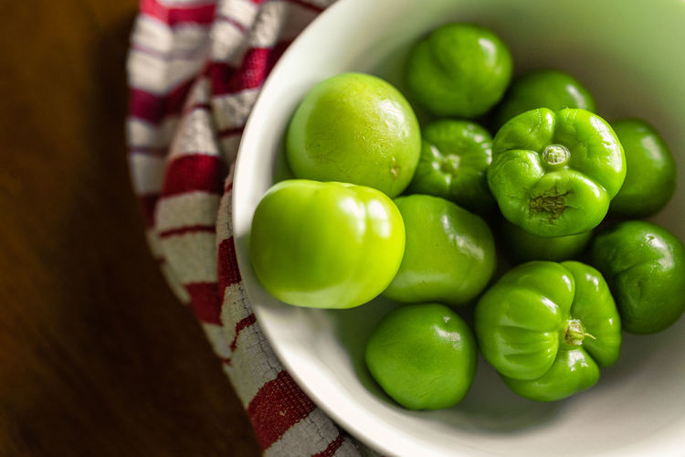 A bowl of fresh tomatillos sitting on a kitchen table