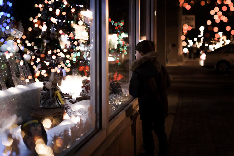 Small young boy looking at christmas decorations inside a store window