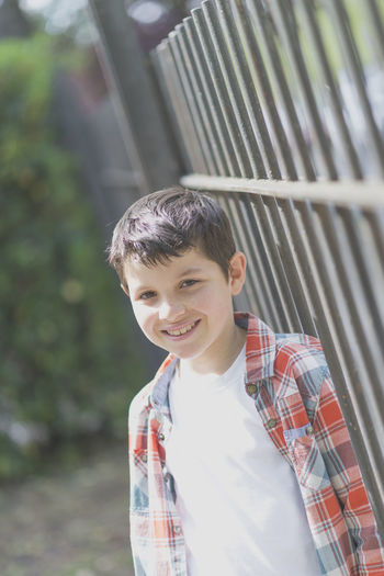 Portrait of boy smiling while standing by railing at park