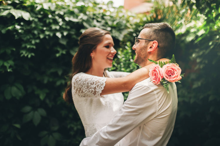 Side view of couple embracing while standing against plants