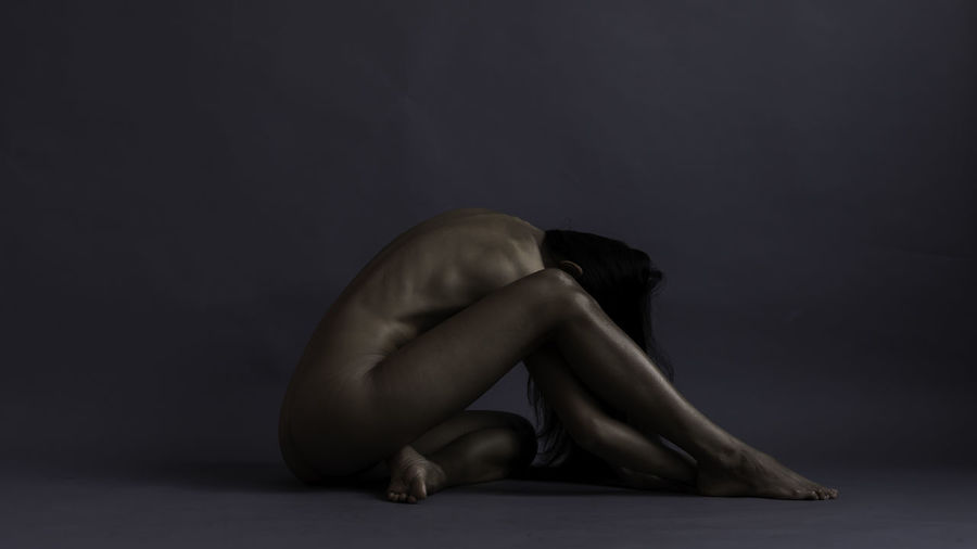 Side view of woman sitting against black background