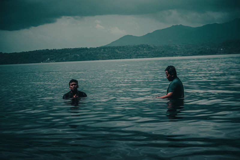 Asian men swimming in lake ranau with mountain views, ranau indonesia.