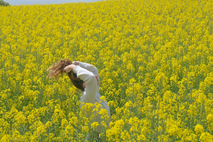 Close-up of woman standing amidst yellow flowering plants on field