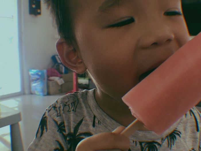 Close-up of boy eating popsicle while standing at home