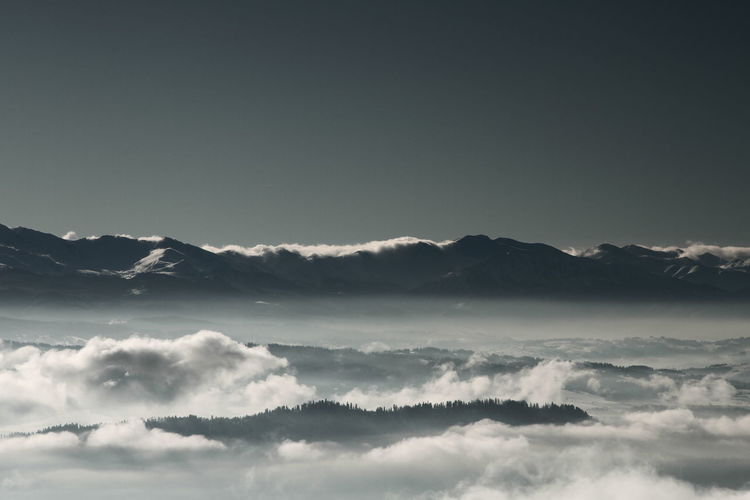 Scenic view of cloud covered mountains against clear sky at dusk