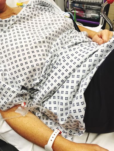 Midsection of woman with iv drip lying on bed in hospital
