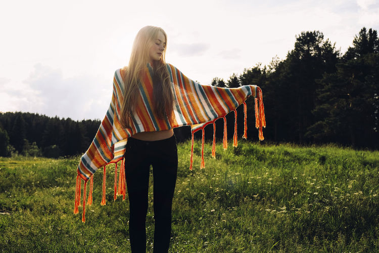 Relaxed woman wearing poncho while standing on grassy field