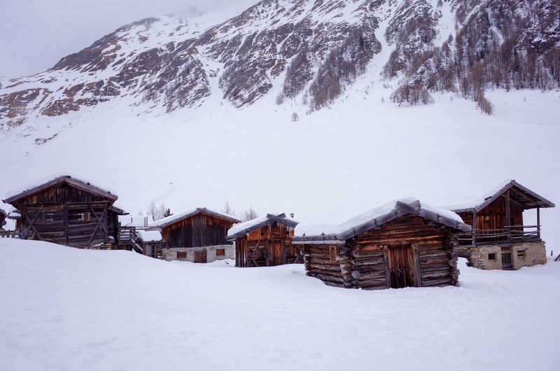 Houses on snow covered field against snowcapped mountains