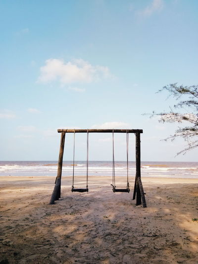 Empty swings at beach against sky