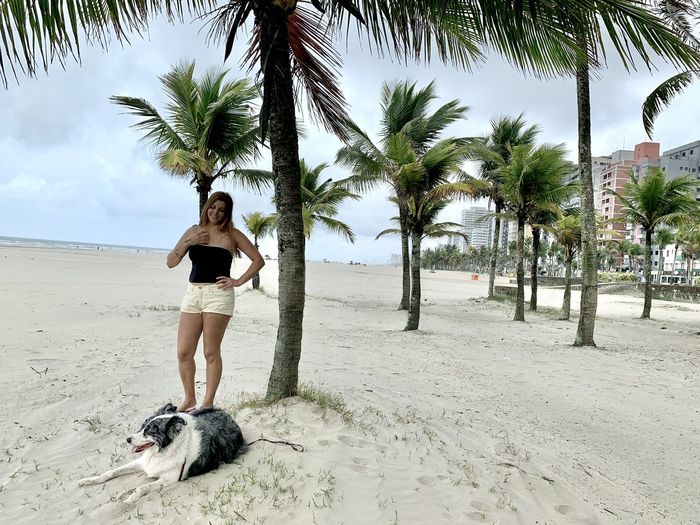 Smiling woman looking at dog while standing on sand