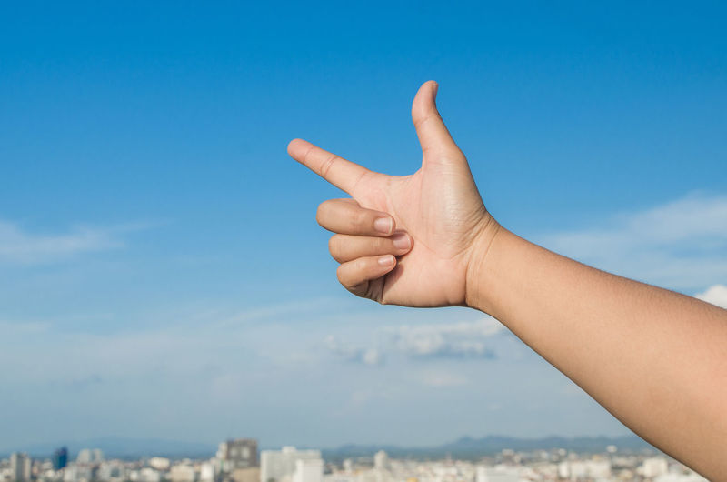 Cropped human hand pointing against sky