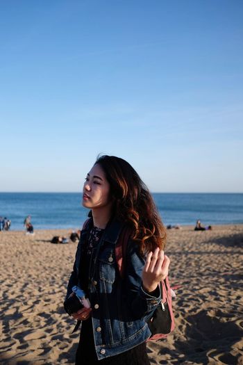 Young woman standing on beach against sky