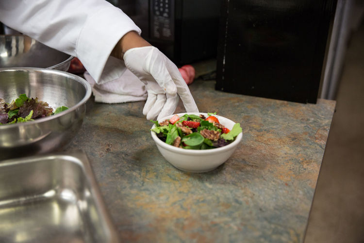 Cropped hand of chef by food bowl in kitchen at restaurant