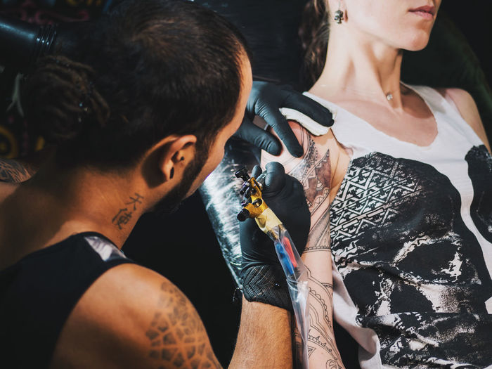 Tattoo artist making tattoo on hand of female customer
